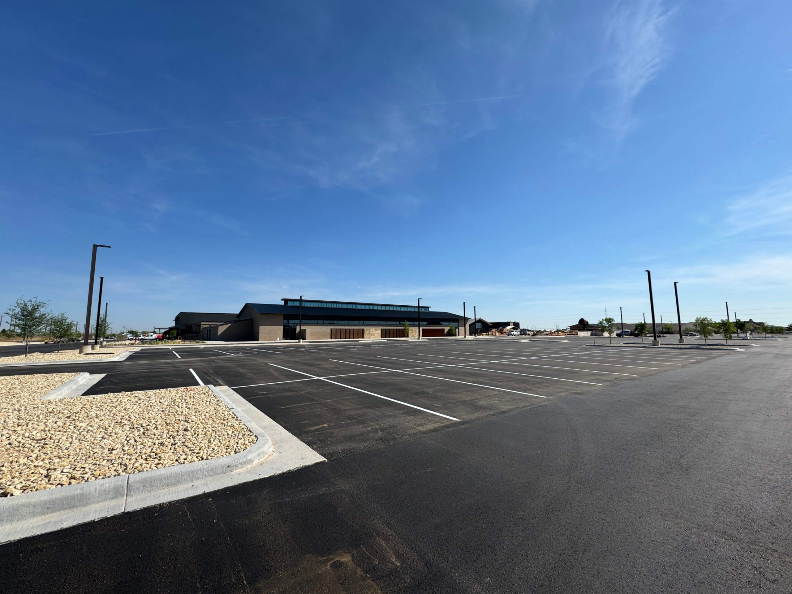 A newly paved and marked commercial asphalt parking lot with clean lines and landscaped edges under a clear blue sky.