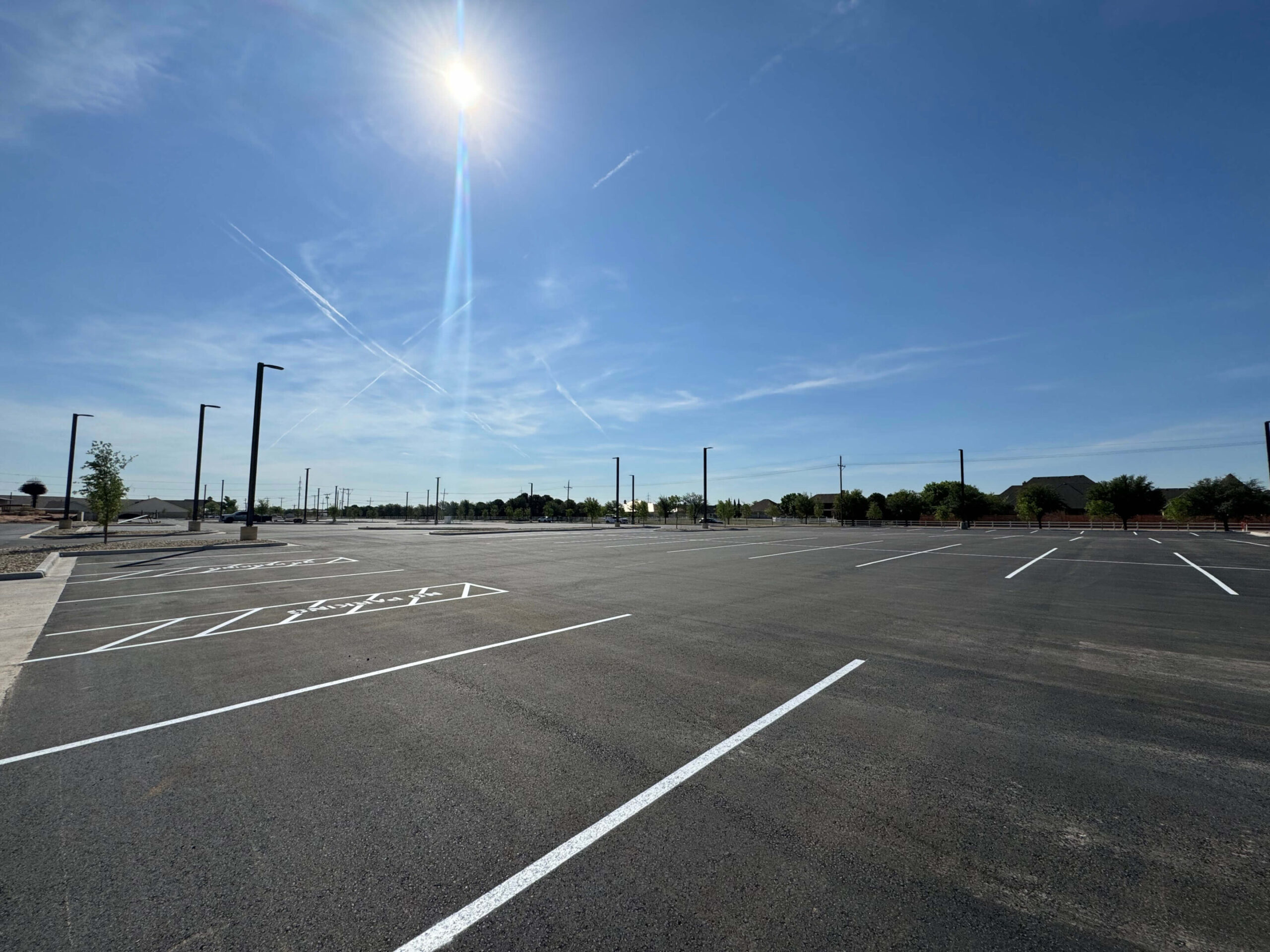 A freshly paved and marked commercial asphalt parking lot under a clear, sunny sky, ready for use.